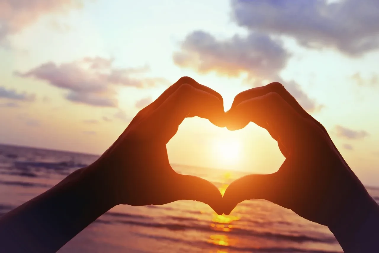 Hands forming a heart shape at sunset on the beach